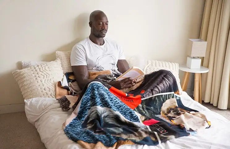 A man reads with a Printerpix custom blanket with dog collage design across his lap.