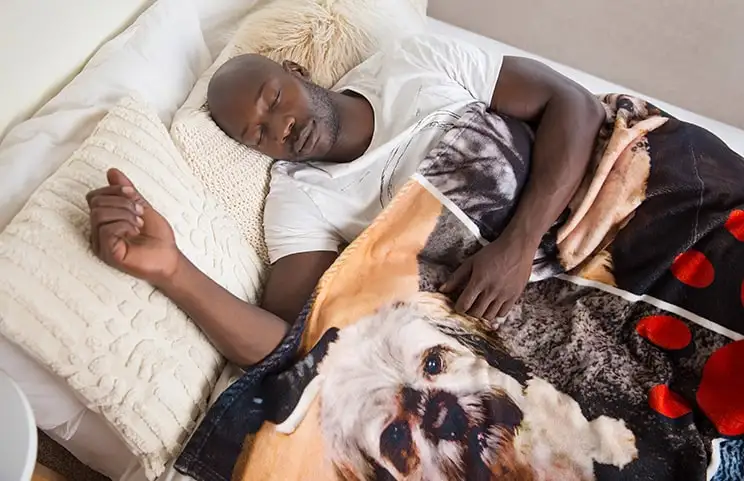 A man sleeps on the bed under a custom Printerpix blanket with dog-design.